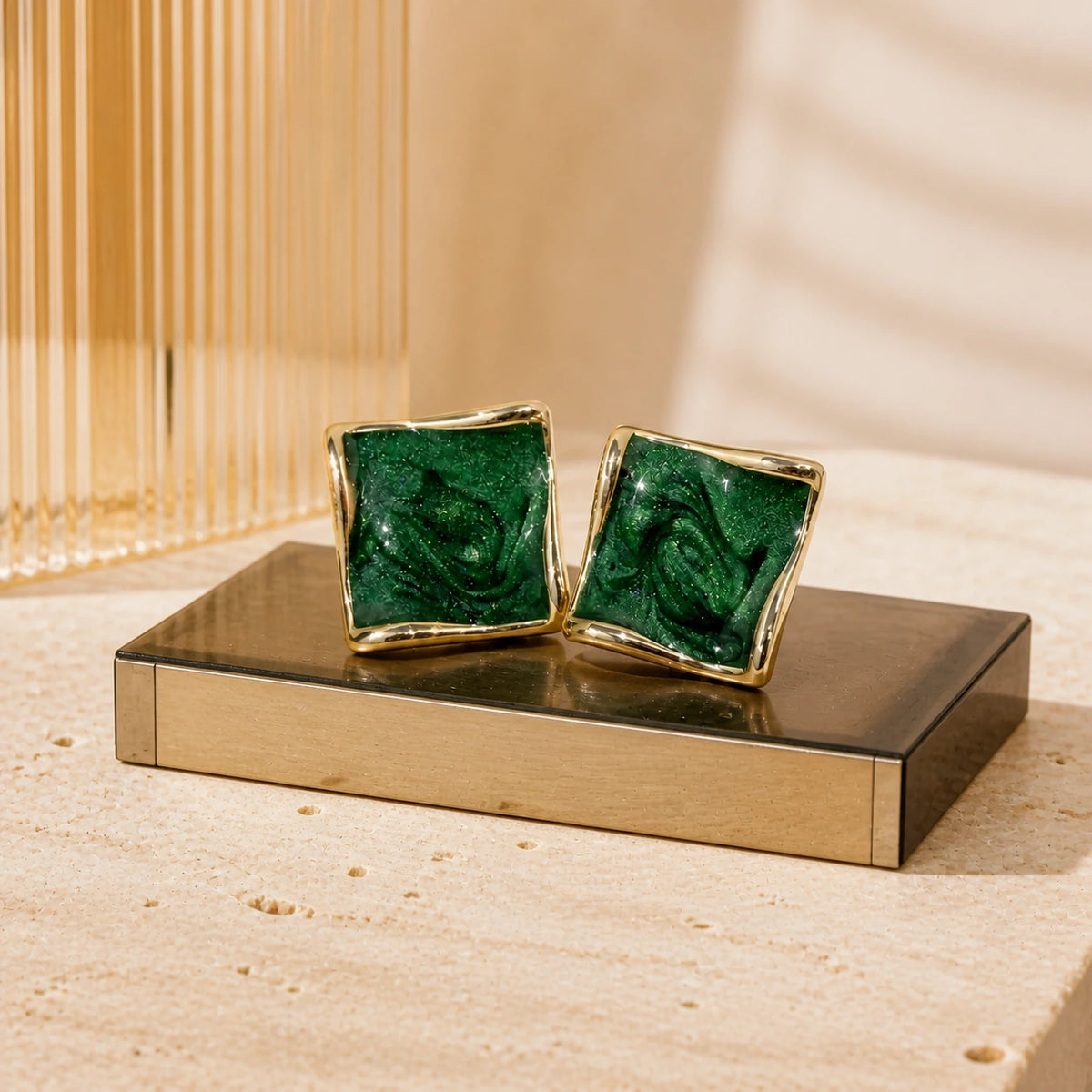 Deep green square stud earrings in gold on modern retro display plinth