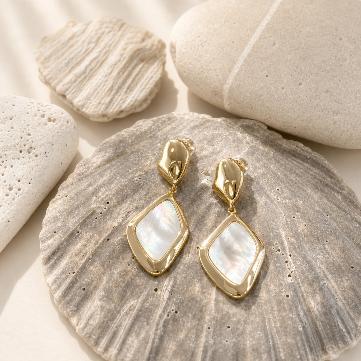Square mother-of-pearl drop earrings in gold close-up on a grey shell-textured plate.