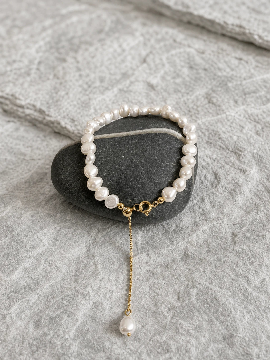 White baroque freshwater pearl bracelet with gold clasp and pearl drop on dark stone