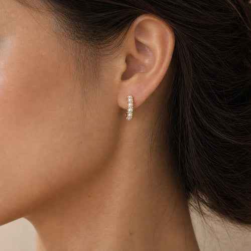 Close-up of mini pearl huggie earrings in Gold-plated brass with 925 sterling silver posts.